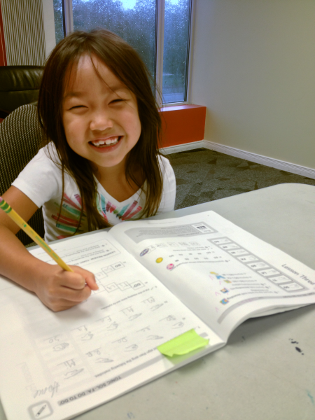 a child with a bright smile writing in her workbook